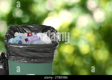 Contenitore per rifiuti con sacchetto di plastica pieno di rifiuti su sfondo sfocato, spazio per testo Foto Stock