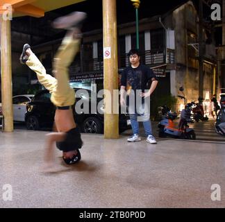 Giovani atleti prendono parte a una festa di gruppo di danza, qui uno di loro sta facendo una break dance "upside down" atletica, a Nakhon Phanom, Isaan, Thailandia, Sud Est Asiatico. Il luogo è la Vietnam Memorial Clock Tower , una torre dell'orologio costruita dai vietnamiti per mostrare il buon rapporto tra Thailandia e Vietnam quando gli immigrati vietnamiti si trasferirono a Nakhon Phanom per vivere in quella provincia. Il locale è all'aperto e gratuito per chiunque. Foto Stock