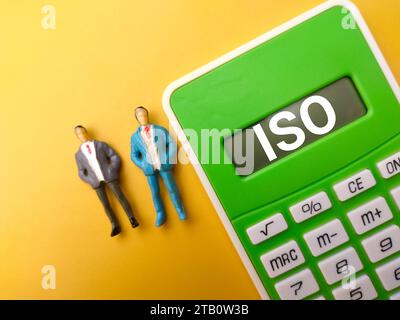 Vista dall'alto in miniatura persone e calcolatrice con testo ISO su sfondo giallo. Foto Stock