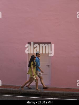 Singapore - 6 maggio 2023: Una coppia asiatica passa una porta sul muro rosa ad Ann Siang Hill, Chinatown, Singapore. Foto Stock