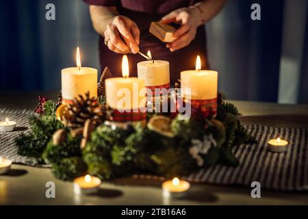 Una donna accende l'ultima quarta candela su una corona d'Avvento durante la vigilia di Natale. Foto Stock