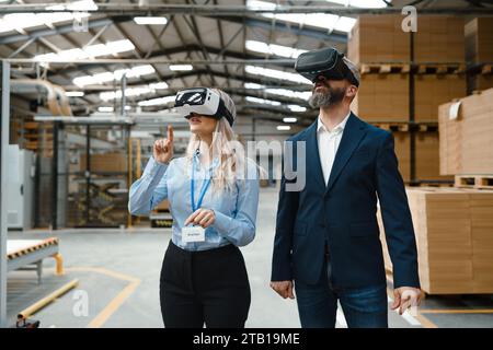 Ingegneri che parlano di progetti utilizzando la realtà virtuale, in una moderna fabbrica industriale. Realtà virtuale nel settore manifatturiero, occhiali intelligenti, AR guida donne e uomini Foto Stock