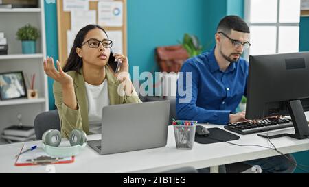 In ufficio, due lavoratori pieni di energia, uomo e donna, impegnati attivamente in una riunione di squadra su un computer, parlando in modo sfrenato sullo smartphone, prospero io Foto Stock