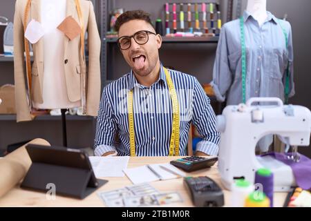 Uomo ispanico con il designer della barba che lavora in un atelier che si sporca la lingua felice di una divertente espressione. concetto di emozione. Foto Stock