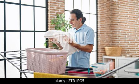 Uomo di mezza età che tiene i vestiti di cesto nella lavanderia Foto Stock