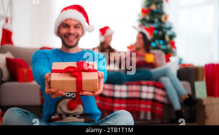 Il ritratto di un bel sorridente in un cappello di Babbo Natale con un regalo di Natale in mano sta potendo e guardando in macchina fotografica. Buon Natale e felice anno nuovo Foto Stock
