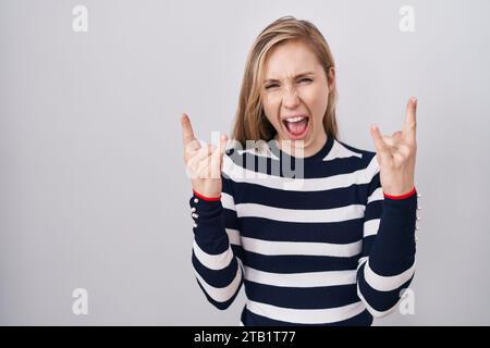 Giovane donna caucasica che indossa un maglione navy casual che urla con un'espressione pazzesca facendo il simbolo del rock con le mani alzate. star della musica. concetto pesante. Foto Stock