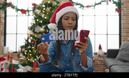 Donna afro-americana che fa shopping con smartphone e carta di credito per festeggiare il natale, sembra sconvolta a casa Foto Stock