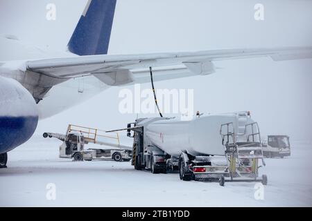 Rifornimento di aeroplano da una autocisterna all'aeroporto durante le nevicate. Servizio a terra prima del volo in una gelida giornata invernale. Foto Stock