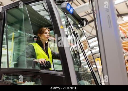 Lavoratrice di magazzino che guida un carrello elevatore a forche. Addetto al magazzino che prepara i prodotti per il mennt, consegna, controllo delle scorte in magazzino. Foto Stock