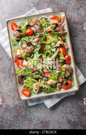 Insalata di fegato di pollo fresco fritto con rucola, cipolle, pomodori, crostini e pancetta da vicino in un piatto su un tavolo. Vista dall'alto verticale Foto Stock