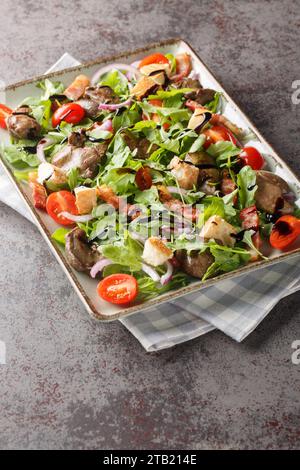 Insalata di fegato di pollo fresco fritto con rucola, cipolle, pomodori, crostini e pancetta da vicino in un piatto su un tavolo. Verticale Foto Stock