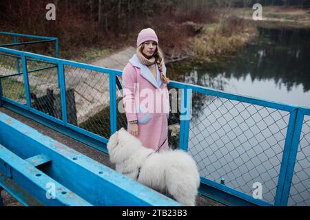 La giovane ragazza cammina con un cane Samoyed bianco e soffice in natura Foto Stock