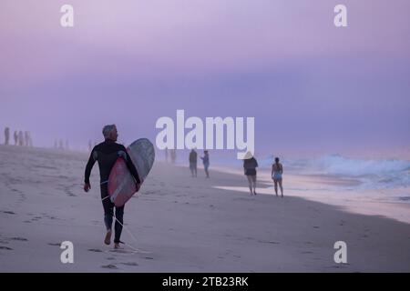 Un surfista anziano cammina sulla spiaggia con la sua tavola da surf a Cape Cod Foto Stock