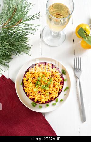 Aringhe vestite, aringhe sotto il cappotto di pelliccia. Insalata Shuba di verdure a strati natalizia con aringhe e verdure bollite. Sfondo di legno bianco. Vista dall'alto Foto Stock