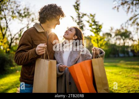 Ritratto di una coppia felice e amorevole al tramonto nel parco. Stanno guardando dentro le borse della spesa. Foto Stock
