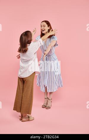 una donna felicissima ed elegante che abbraccia la figlia adolescente su uno sfondo rosa, unity Foto Stock