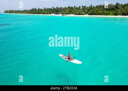 Veduta aerea di una donna su una tavola bianca nelle acque turchesi delle Maldive Foto Stock