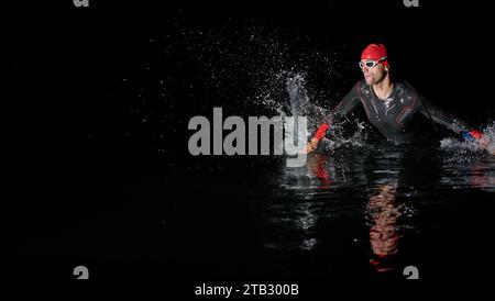 Un triatleta professionista determinato è sottoposto a rigorosi allenamenti notturni in acque fredde, dimostrando dedizione e resilienza in preparazione di un Foto Stock