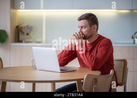 Un uomo stressato e preoccupato siede con un notebook che si sente burnout, apatia, problemi di concentrazione a casa. Foto Stock