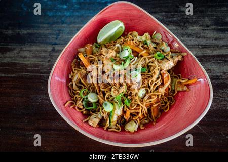 Una ciotola di noodle di pollo e verdure in stile thailandese servita in una ciotola rossa. Foto Stock