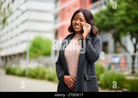 Giovane donna nera che indossa ufficialmente una telefonata mentre cammina fuori Foto Stock