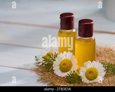 Olio aromatico con camomilla. Bottiglia di olio essenziale e fiori di camomilla sul tavolo Foto Stock