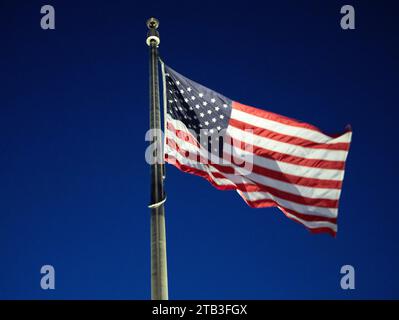 La bandiera degli Stati Uniti d'America, le stelle e le strisce, che soffiano e sventolano nel vento, su un palo della bandiera al crepuscolo Foto Stock