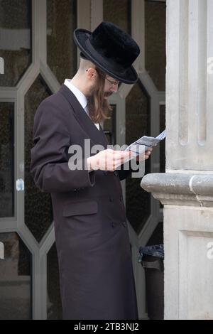 Un ebreo ortodosso con un lungo peyus non ricalcato legge un programma settimanale di conferenze fuori da una sinagoga di Satmar a Brooklyn, New York. Foto Stock