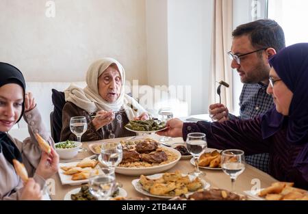 La famiglia araba cena insieme su un tavolo di legno con padre, madre, nonno, nonna e figlio Foto Stock