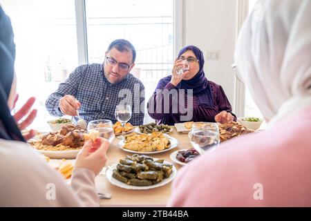 La famiglia araba cena insieme su un tavolo di legno con padre, madre, nonno, nonna e figlio Foto Stock