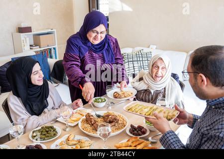 La famiglia araba cena insieme su un tavolo di legno con padre, madre, nonno, nonna e figlio Foto Stock