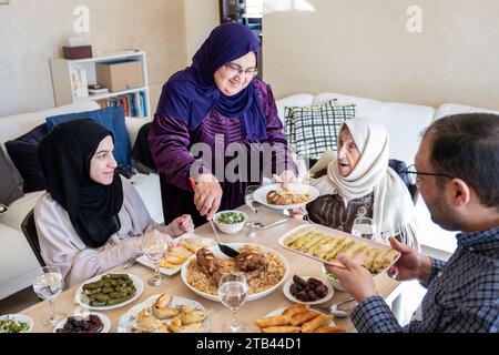 La famiglia araba cena insieme su un tavolo di legno con padre, madre, nonno, nonna e figlio Foto Stock