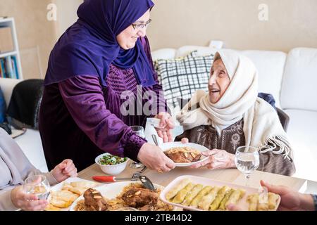 La famiglia araba cena insieme su un tavolo di legno con padre, madre, nonno, nonna e figlio Foto Stock