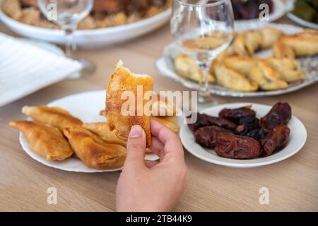 Porta a mano un pezzo di qatayef su un tavolo di legno con datteri Foto Stock