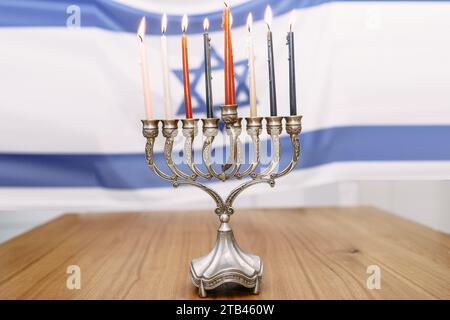 Hanukkah Menorah illuminando il tavolo di legno, celebrando il Festival delle luci con otto candele e Shamash, sullo sfondo della bandiera israeliana in bianco e blu, adornato con Magen David Foto Stock