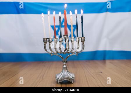 Hanukkah Menorah illuminando il tavolo di legno, celebrando il Festival delle luci con otto candele e Shamash, sullo sfondo della bandiera israeliana in bianco e blu, adornato con Magen David Foto Stock