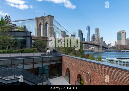 New York City, NY, USA-10 ottobre 2023: Vista dal basso angolo del ponte di Brooklyn con Lower Manhattan sullo sfondo e il parco sul tetto Empire Stores di fronte Foto Stock