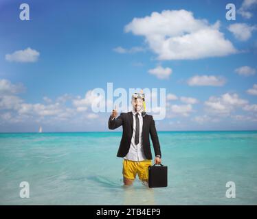 Uomo d'affari con una maschera subacquea in mare con in mano una valigetta e con i pollici in alto Foto Stock
