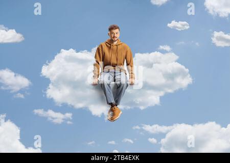 Un ragazzo con un jeans e una felpa con cappuccio seduto su una nuvola in cielo Foto Stock