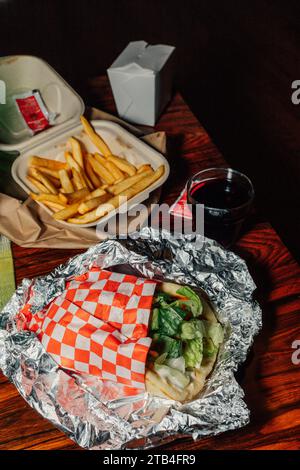 Pasto da asporto con shawarma di pollo, patatine fritte, pacchetti "ketchup di pomodoro" e bicchiere di vino rosso su tavola di legno Foto Stock