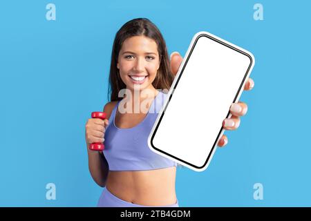 Fit Woman in sportswear mostra un enorme schermo vuoto dello smartphone, studio Foto Stock