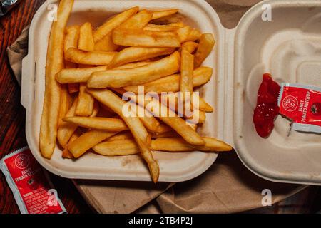 Scatola di carta con patatine fritte da asporto con pacchetti di "ketchup di pomodoro fantasioso" su sacchetto di carta marrone Foto Stock