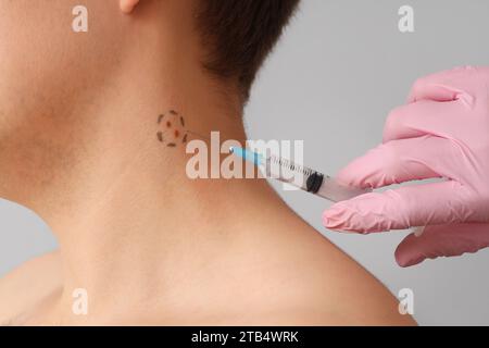 Dermatologo che prende puntura mole da giovane su sfondo chiaro, primo piano Foto Stock