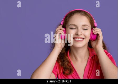 Ritratto di una giovane donna rilassata che ascolta musica su sfondo viola Foto Stock