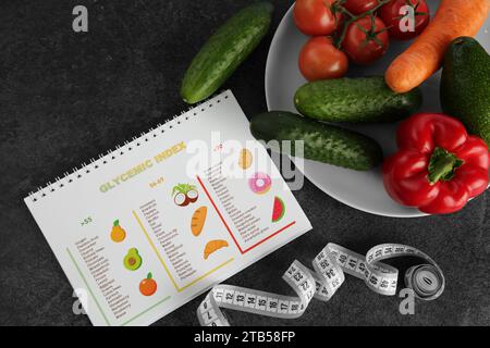 Notebook con informazioni sull'indice glicemico, il metro a nastro e le verdure su un tavolo grigio, piatto Foto Stock