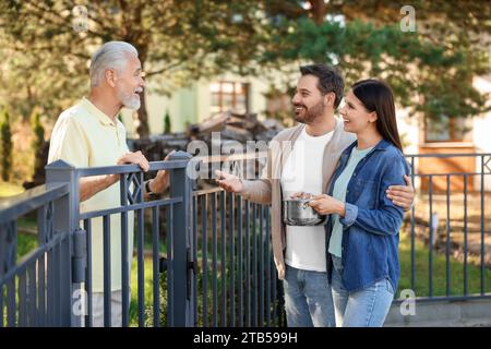 Rapporto amichevole con i vicini. Coppia felice e uomo anziano vicino alla recinzione all'aperto Foto Stock