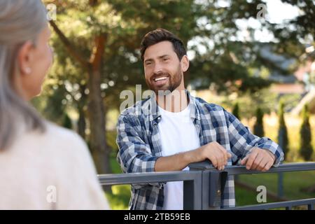 Rapporto amichevole con i vicini. Uomo felice e donna anziana vicino a recinzione all'aperto Foto Stock