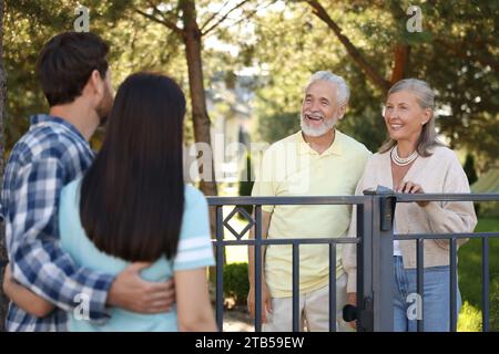 Rapporto amichevole con i vicini. Famiglia giovane che parla con coppie anziane vicino a recinzione all'aperto Foto Stock