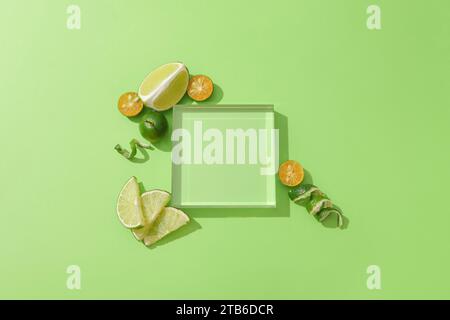 Un podio di vetro trasparente è collocato su uno sfondo verde, circondato da limoni freschi e kumquat. Podio vuoto per esporre prodotti naturali. Foto Stock